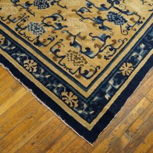 Low-pile gold rug with dark blue stylized floral motifs and borders on distressed wood floor.