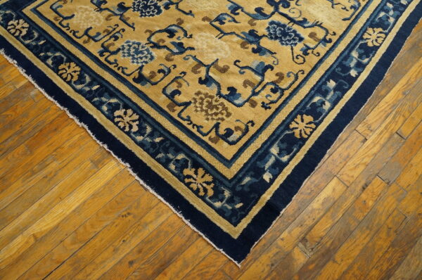 Low-pile gold rug with dark blue stylized floral motifs and borders on distressed wood floor.