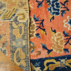 Detail of a rug showing the woven backing and the coral pile face with blue and yellow florals on wood floor.