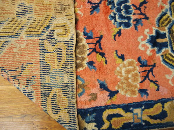 Detail of a rug showing the woven backing and the coral pile face with blue and yellow florals on wood floor.