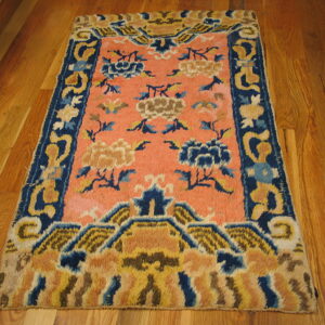 High-pile coral rug featuring large blue and gold floral motifs and an elaborate blue border on wood planks.