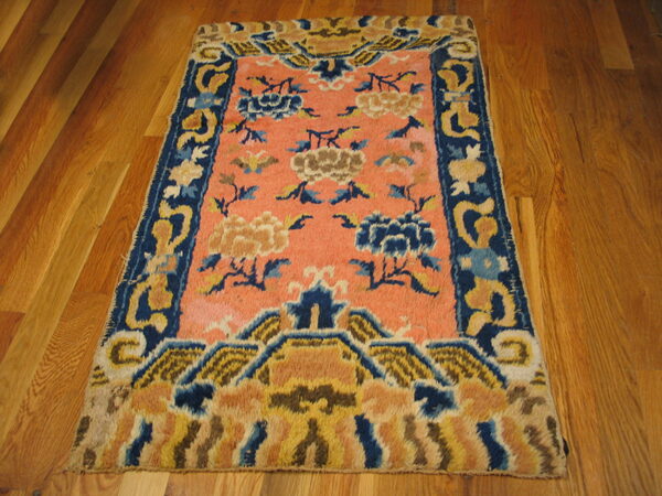 High-pile coral rug featuring large blue and gold floral motifs and an elaborate blue border on wood planks.