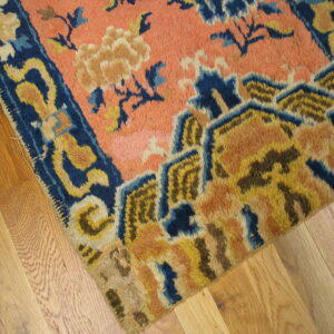 Coarse-pile rug in salmon, indigo, and gold patterns lays across light hardwood planks.