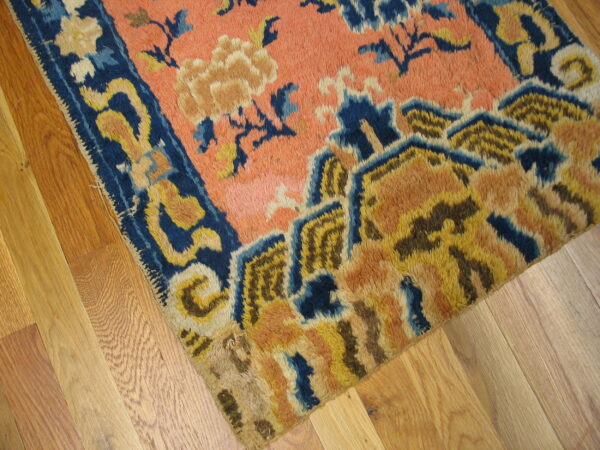 Coarse-pile rug in salmon, indigo, and gold patterns lays across light hardwood planks.