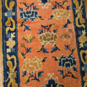 A low pile rug featuring blue and gold floral designs on a salmon-colored field over hardwood.