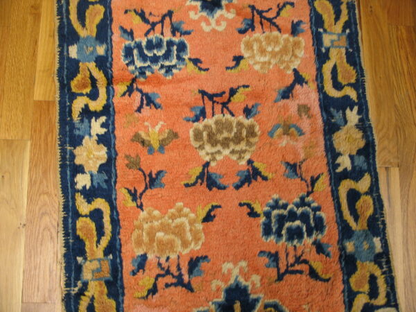 A low pile rug featuring blue and gold floral designs on a salmon-colored field over hardwood.
