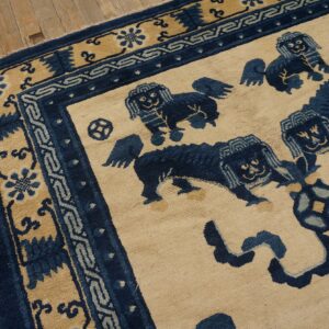 Beige rug featuring a dark blue stylized lion pattern and intricate borders on rustic wood flooring.
