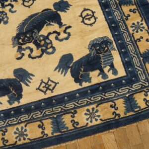 Tan and navy rug with stylized lion figures and decorative borders rests on wooden plank flooring.