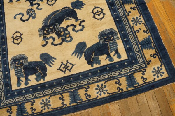Tan and navy rug with stylized lion figures and decorative borders rests on wooden plank flooring.