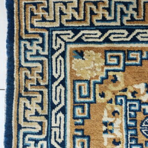 Geometric rug border in dark blue, tan, and cream sits on white tiled flooring.