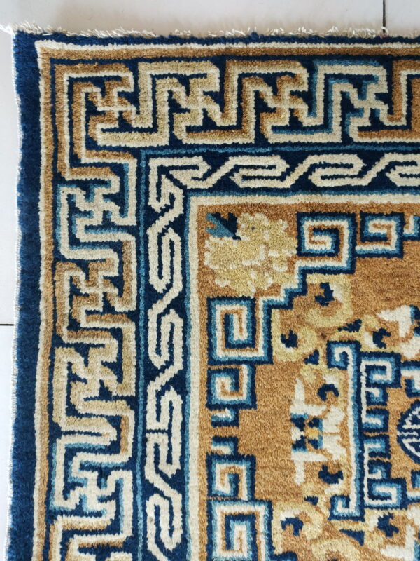 Geometric rug border in dark blue, tan, and cream sits on white tiled flooring.