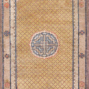 Gold field rug with a circular geometric medallion and angular blue-and-tan stepped borders.