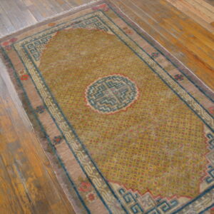 Mustard yellow rug with a central medallion and teal and mauve geometric borders on wood flooring.