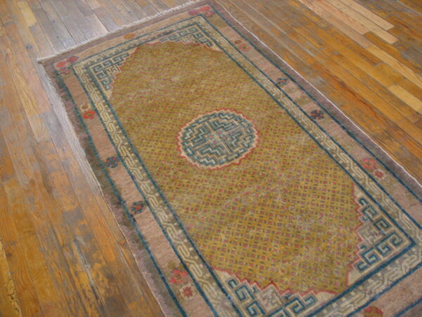 Mustard yellow rug with a central medallion and teal and mauve geometric borders on wood flooring.