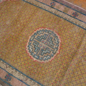 Close-up of a distressed gold runner with a blue geometric medallion and rose border on wood flooring.