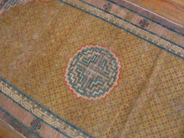 Close-up of a distressed gold runner with a blue geometric medallion and rose border on wood flooring.