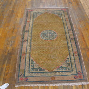 Gold and brown geometric rug with a blue border displayed on distressed wood plank floors.