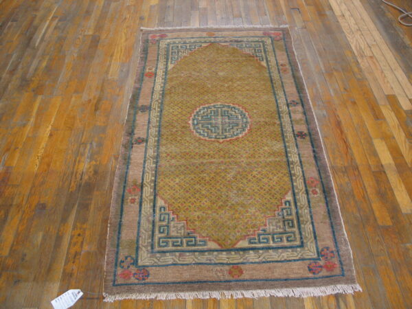 Gold and brown geometric rug with a blue border displayed on distressed wood plank floors.