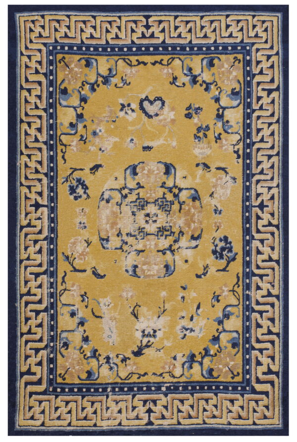 Gold rug with distressed blue and tan floral motifs bordered by a navy blue geometric greek key design.