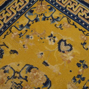 A mustard yellow rug featuring faded floral designs and a sharp blue and tan geometric border rests on wood flooring.