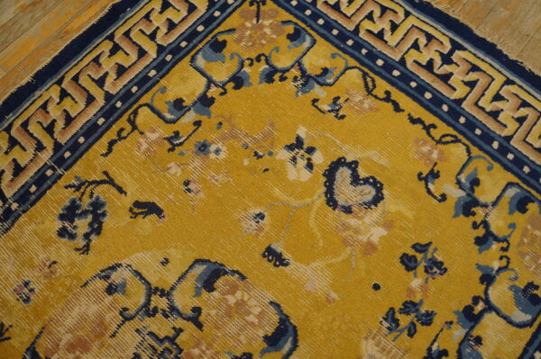 A mustard yellow rug featuring faded floral designs and a sharp blue and tan geometric border rests on wood flooring.
