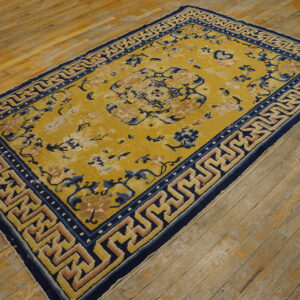 Yellow floral rug featuring a bold navy blue and tan geometric key border on wide hardwood planks.