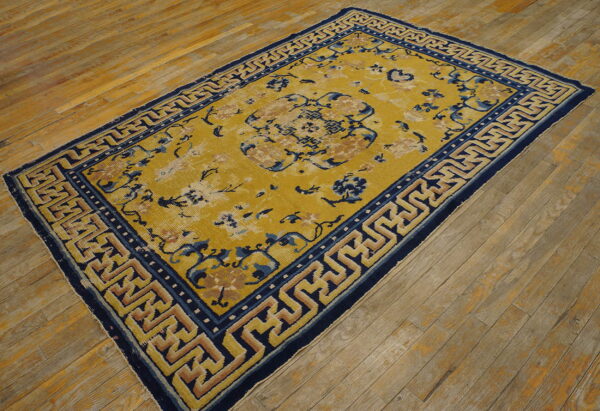 Yellow floral rug featuring a bold navy blue and tan geometric key border on wide hardwood planks.