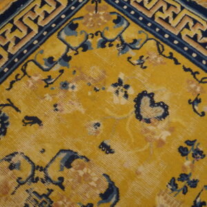 Close-up of a yellow rug with navy blue floral and geometric patterns visible on a distressed wood floor.