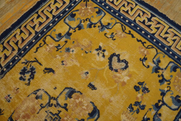 Close-up of a yellow rug with navy blue floral and geometric patterns visible on a distressed wood floor.