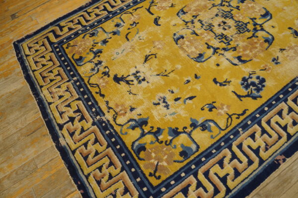 Mustard yellow rug with navy and tan floral and fret patterns on distressed wooden floor.