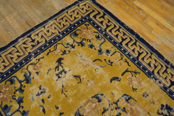 Distressed gold rug with navy blue floral patterns and geometric borders rests on light wood planks.
