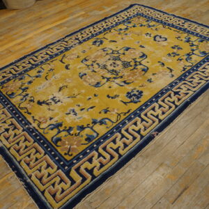 Worn gold rug with blue floral and tan geometric patterns rests on rustic hardwood floors.