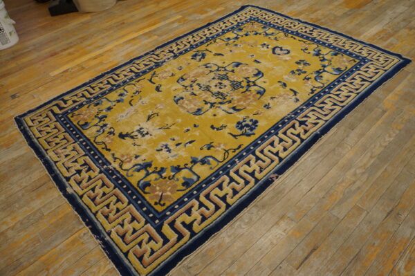 Worn gold rug with blue floral and tan geometric patterns rests on rustic hardwood floors.