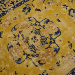 Mustard yellow rug with blue, tan, and faded floral patterns sits against hardwood flooring.