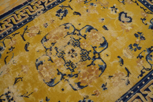 Mustard yellow rug with blue, tan, and faded floral patterns sits against hardwood flooring.