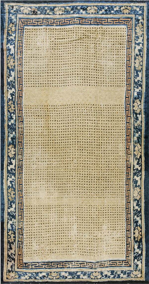 The beige rug features a fine repeating diamond pattern bordered by intricate navy blue floral and fret designs.
