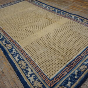 A large distressed beige rug with a blue and peach geometric border rests on rustic wooden floorboards.