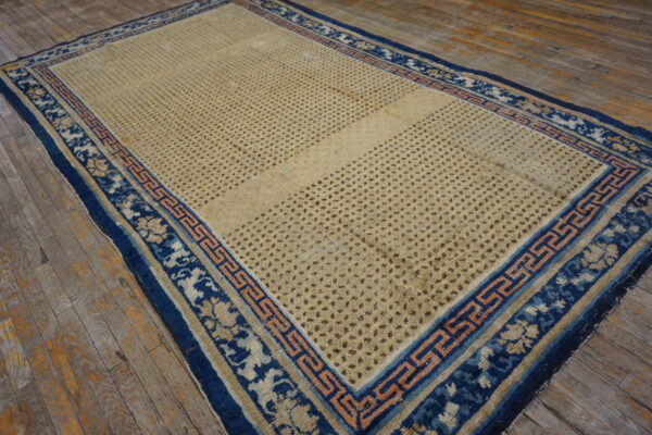 A large distressed beige rug with a blue and peach geometric border rests on rustic wooden floorboards.