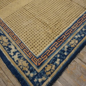 Beige rug corner featuring a dotted texture and a layered blue and peach geometric border on wood flooring.