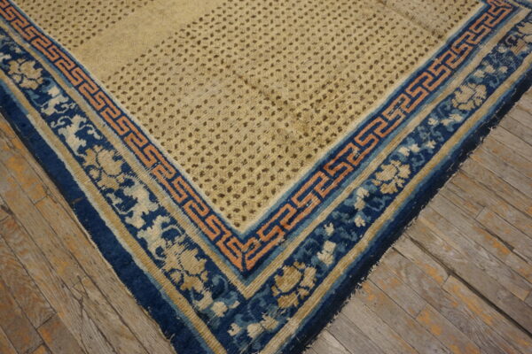 Beige rug corner featuring a dotted texture and a layered blue and peach geometric border on wood flooring.