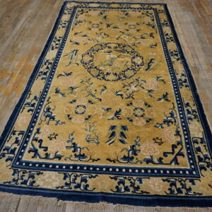 Gold rug with navy borders and pink floral patterns lies on light brown distressed wood planks.