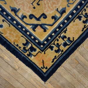Plush golden-yellow and navy blue rug corner with peach accents rests on weathered hardwood flooring.