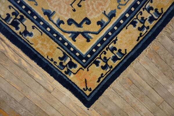Plush golden-yellow and navy blue rug corner with peach accents rests on weathered hardwood flooring.