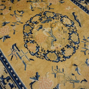 A gold and navy blue rug with a dense floral and medallion pattern sits on wood floorboards.