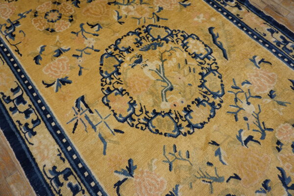 A gold and navy blue rug with a dense floral and medallion pattern sits on wood floorboards.