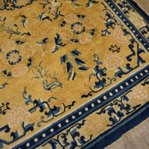Mustard yellow rug with navy blue and pale pink stylized floral and vine patterns on wood flooring.