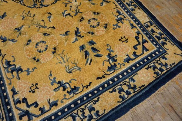 Mustard yellow rug with navy blue and pale pink stylized floral and vine patterns on wood flooring.