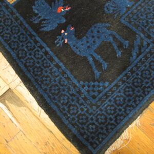 Close-up of a dark rug featuring blue animal and bird motifs, framed by a geometric border on hardwood flooring.