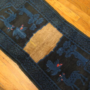 Black runner rug featuring blue animal patterns, a geometric border, and a large central tan patch of damage on a wood floor.