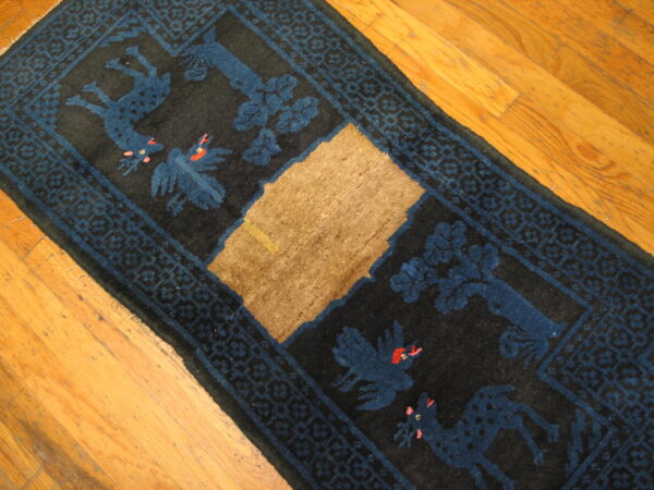 Black runner rug featuring blue animal patterns, a geometric border, and a large central tan patch of damage on a wood floor.